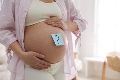Pregnant woman with sticky note on belly at home, closeup. Choosing baby name