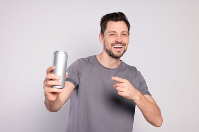 Happy man holding tin can with beverage on light grey background