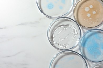 Photo of Petri dishes with liquids on white marble table, flat lay. Space for text
