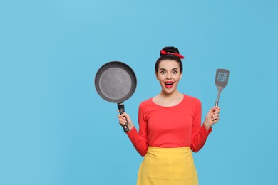 Photo of Emotional housewife with frying pan and spatula on light blue background. Space for text