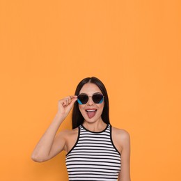 Attractive happy woman in fashionable sunglasses showing tongue against orange background. Space for text