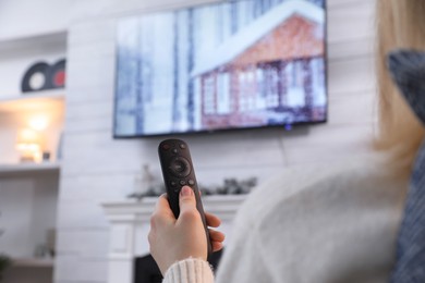 Woman with remote control watching TV at home, closeup