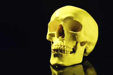 Yellow human skull on black background, space for text