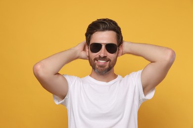 Portrait of smiling bearded man with stylish sunglasses on orange background