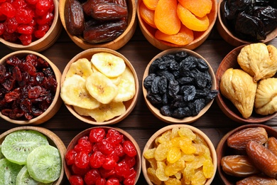 Bowls with different dried fruits on wooden background, flat lay. Healthy lifestyle