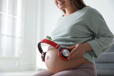 Pregnant woman with headphones on her belly indoors, closeup