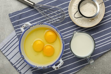 Whisk, eggs, milk and flour on grey table, flat lay