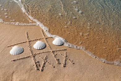 Playing Tic tac toe game with shells on sand near sea, above view. Space for text