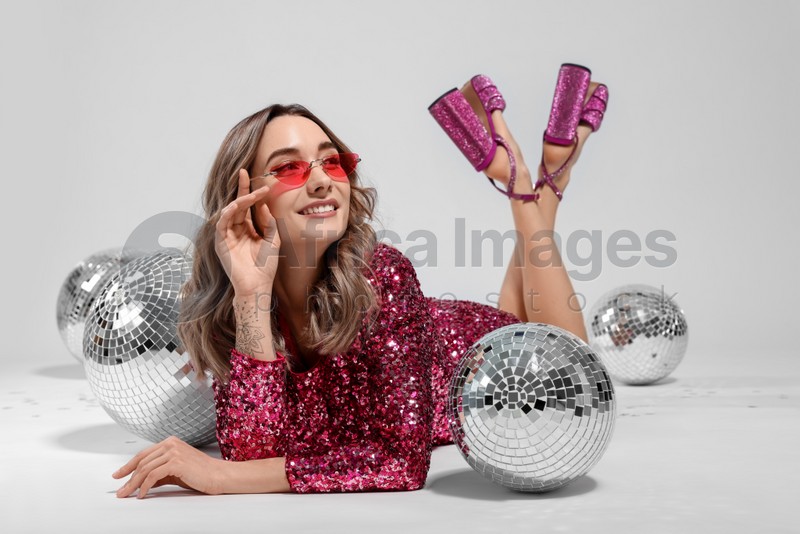 Photo of Beautiful woman in sunglasses and sequin dress among disco balls on white background