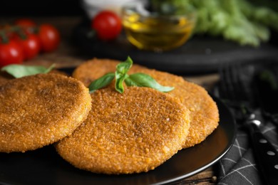 Photo of Delicious fried breaded cutlets with basil on wooden table, closeup