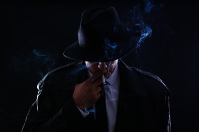 Old fashioned detective smoking cigarette on dark background