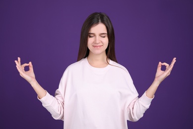 Young woman meditating on purple background. Stress relief exercise