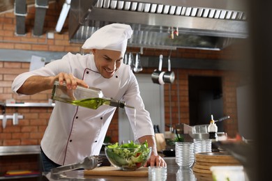 Professional chef pouring oil into bowl with fresh salad in restaurant kitchen, space for text