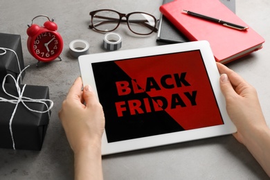 Woman using tablet with Black Friday announcement at grey table, closeup