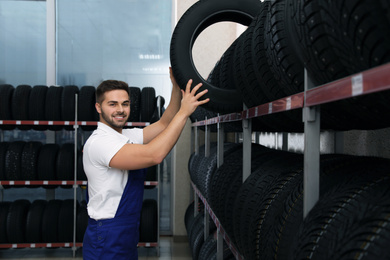Male mechanic with car tire in auto store
