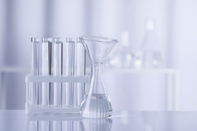Different laboratory glassware with transparent liquid on table against blurred background. Space for text