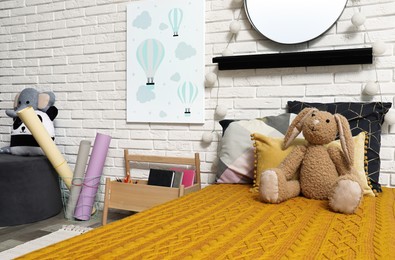 Photo of Cute toy bunny on bed with orange blanket. Bedroom interior