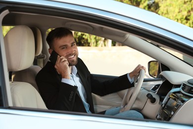 Handsome young driver talking on phone in modern car