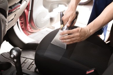 Male worker removing dirt from car seat with professional vacuum cleaner