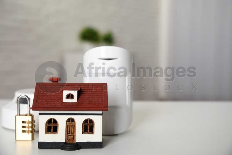 House model, lock, smoke and movement detectors on table in room, space for text. Home security system