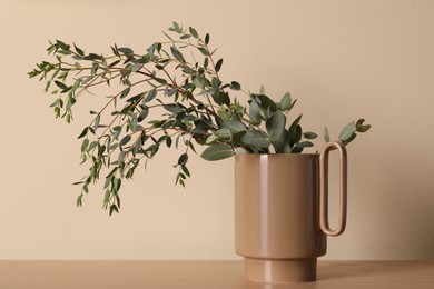 Stylish ceramic vase with eucalyptus branches on wooden table near beige wall