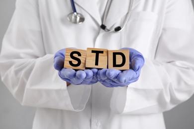 Doctor holding wooden cubes with abbreviation STD on grey background, closeup
