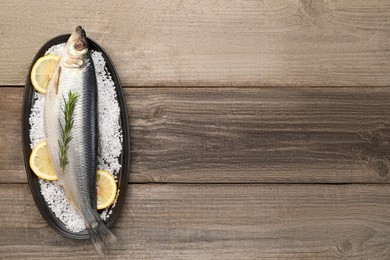 Plate with salted herring, rosemary and lemon on wooden table, top view. Space for text