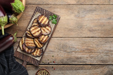 Delicious grilled eggplant slices on wooden table, flat lay. Space for text