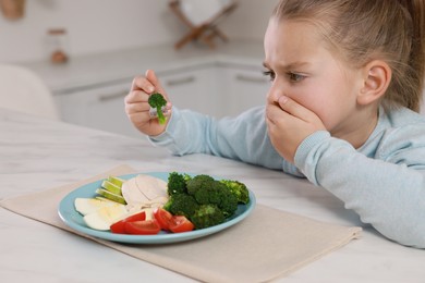 Cute little girl covering mouth and refusing to eat dinner in kitchen