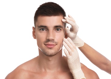 Doctor examining man's face for cosmetic surgery on white background