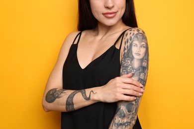 Beautiful woman with tattoos on arms against yellow background, closeup