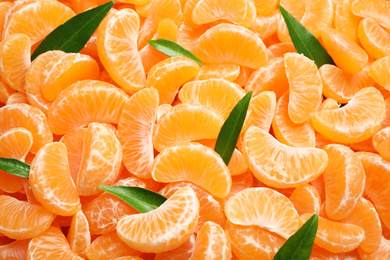 Fresh juicy tangerine segments with green leaves as background, top view