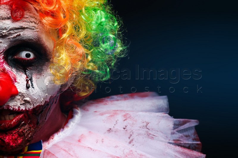 Terrifying clown on dark background, closeup. Halloween party costume