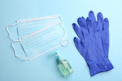 Medical gloves, masks and hand sanitizer on light blue background, flat lay