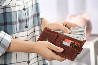 Woman putting money into wallet on blurred background, closeup