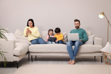 Photo of Happy family with gadgets on sofa in living room