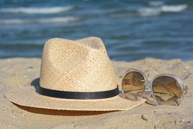 Stylish straw hat and sunglasses on sandy beach