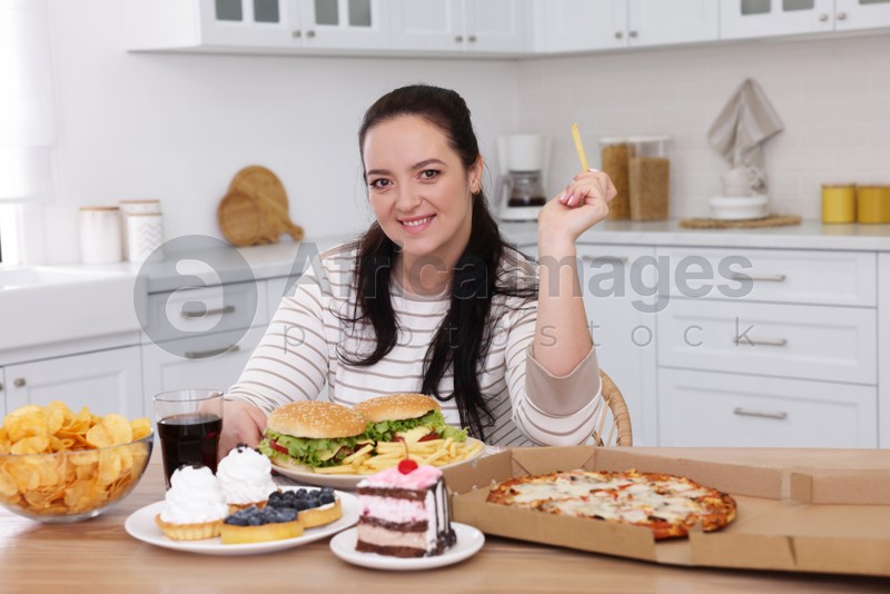Happy overweight woman with unhealthy food in kitchen