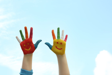 Kid with smiling faces drawn on palms against blue sky, closeup. Space for text