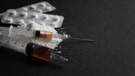 Photo of Syringes, pills and powder on black background, closeup with space for text. Hard drugs