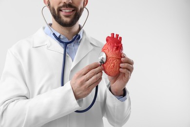 Doctor with stethoscope and model of heart on white background, closeup. Cardiology concept