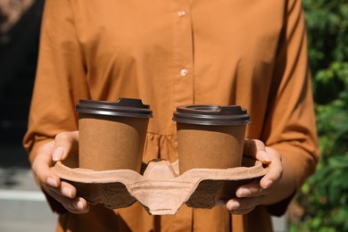 Woman holding takeaway cardboard coffee cups with plastic lids outdoors, closeup