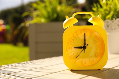 Yellow alarm clock on white wooden table outdoors at sunny morning. Space for text