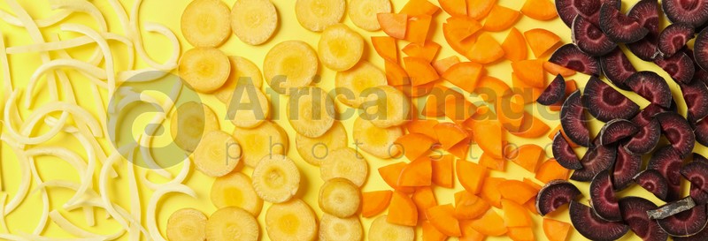 Pieces of raw color carrots on yellow background, flat lay