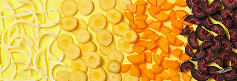 Pieces of raw color carrots on yellow background, flat lay