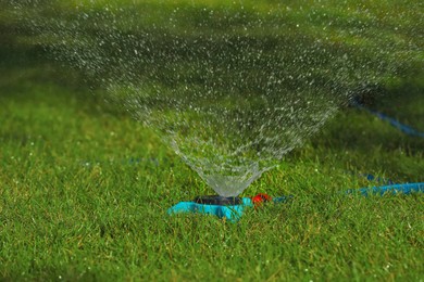 Photo of Automatic sprinkler watering green grass outdoors. Irrigation system
