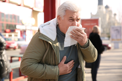 Sick senior man with tissue on city street. Influenza virus