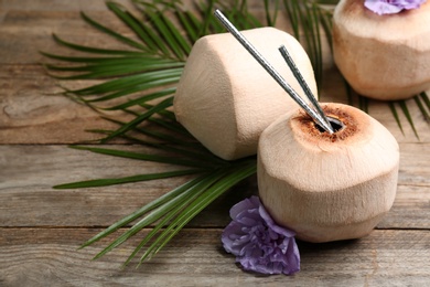 Fresh coconuts with drinking straws and flower on wooden table. Space for text