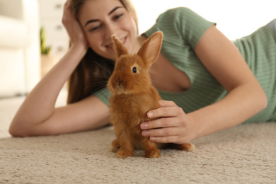 Young woman with adorable rabbit on floor indoors. Lovely pet