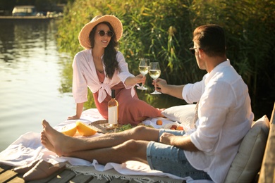 Couple clinking glasses with wine on pier at picnic